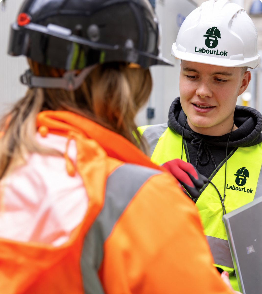 A young worker in LabourLok hi-vis and hard hat talking through the job with a colleague on site