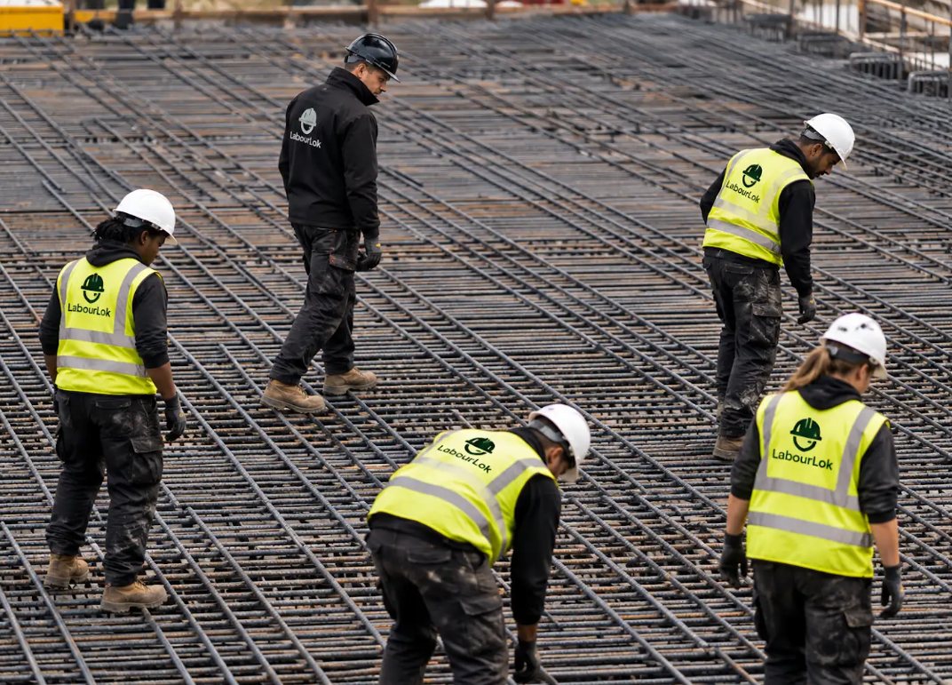 Young LabourLok workers in branded hi-vis and white hard hats on a reinforcement deck with their supervisor