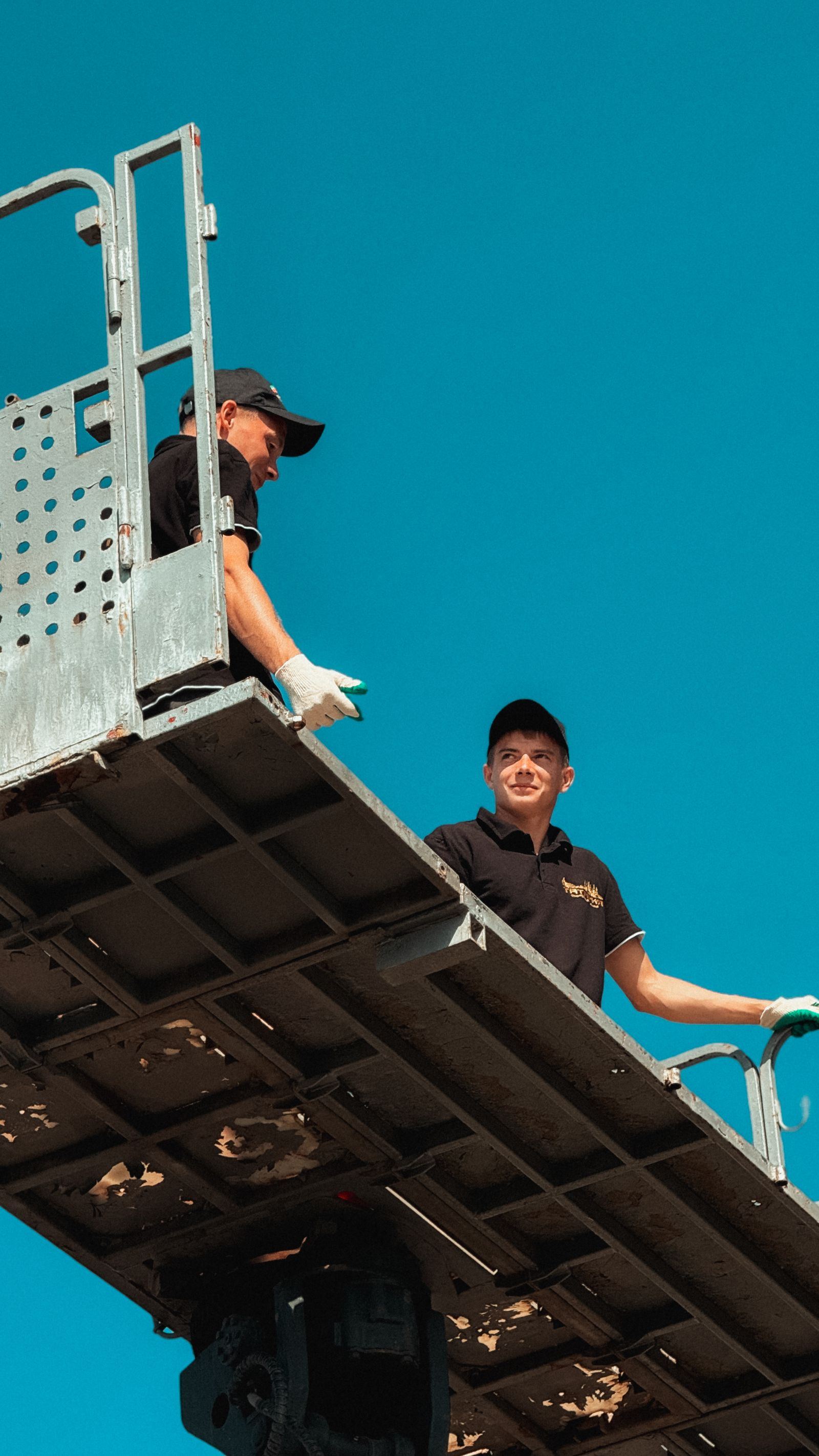 Two workers on an access platform against a blue sky