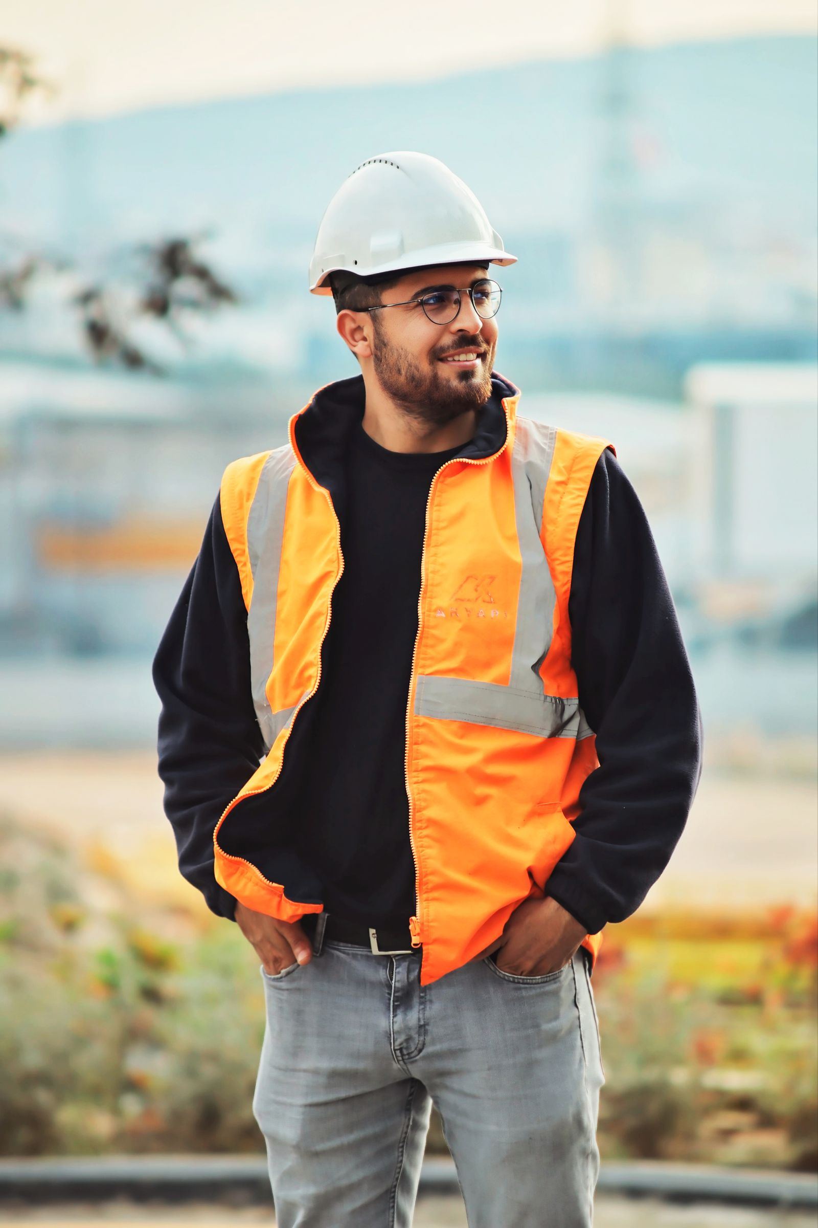 A young worker in an orange hi-vis vest and white hard hat on site